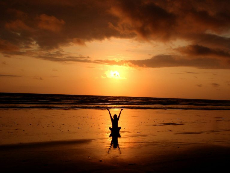 Person practicing yoga on a serene beach at sunset with golden sky and ocean horizon