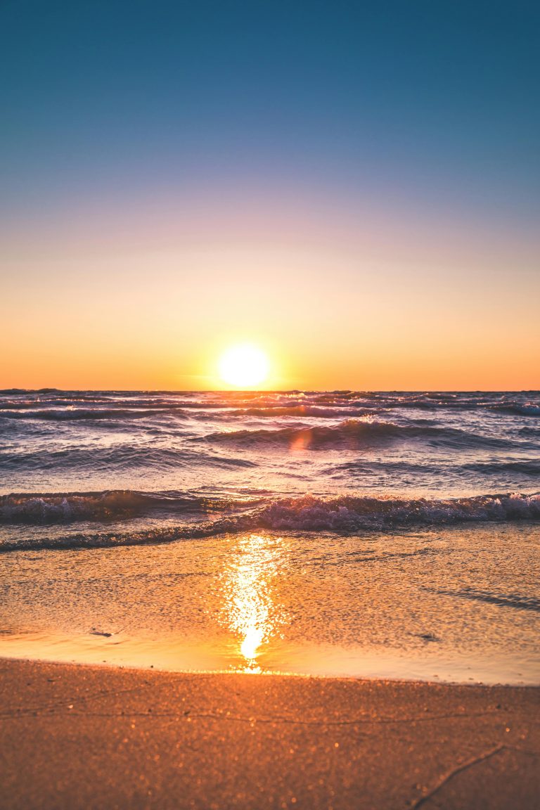 Vibrant sunset over ocean waves with golden light reflecting on sandy beach