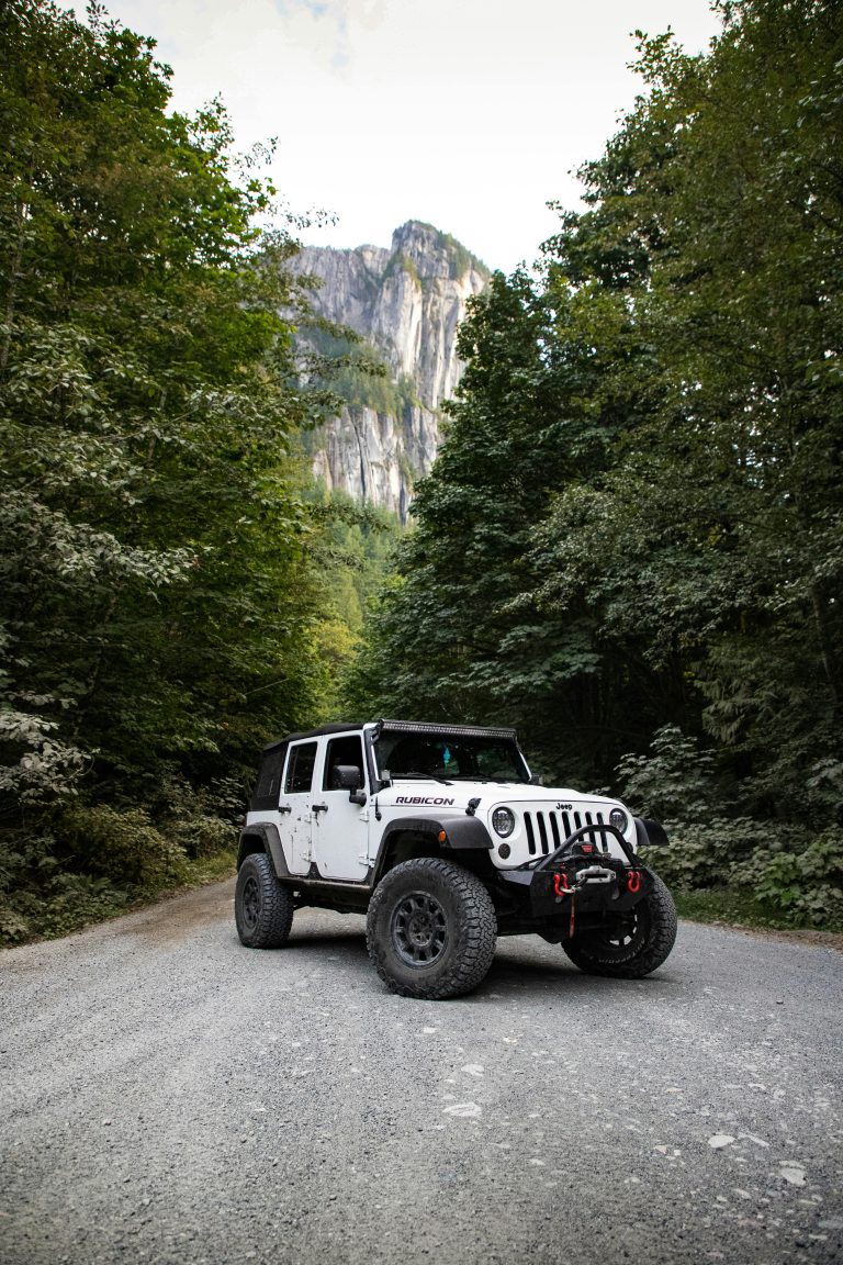 White Jeep Rubicon on a forest trail with a rocky mountain in the background