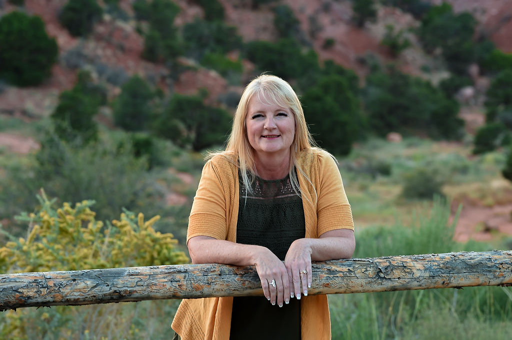 Alissa in a yellow cardigan leaning on a wooden fence with desert background
