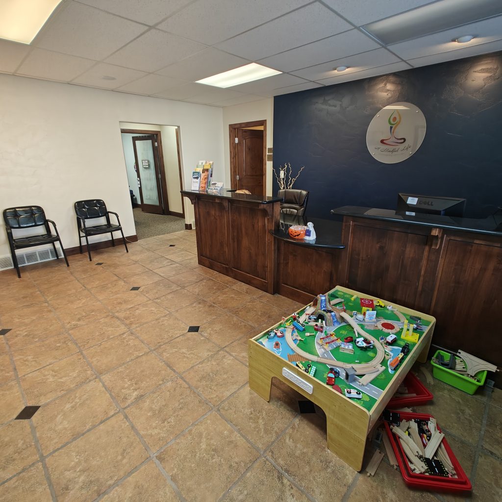 Reception area with wooden desk, chairs, and kids' play table featuring a train set and colorful toys on tiled floor