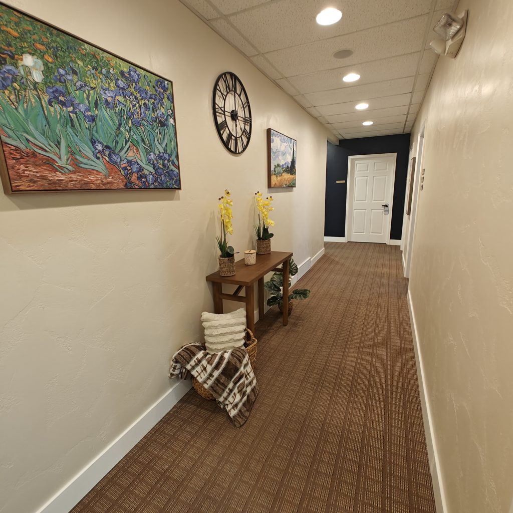 Hallway with modern decor, colorful paintings, wall clock, wooden table, yellow flowers, and a cozy blanket basket